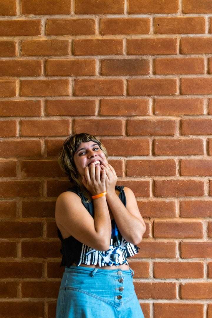 Uma mulher de costas para a câmera, olhando para o fundo, com um canto da parede visível atrás dela.