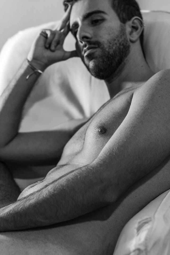 Pessoa de costas sentada em cama, luz suave vinda de uma janela parcialmente aberta.