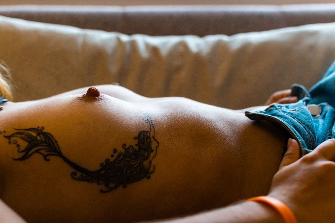 Pessoa de costas sentada em sofá, olhos voltados para a câmera, luz natural suave vindo da janela lateral.
