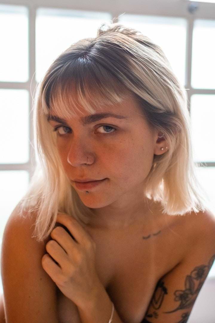 Uma mulher sentada em frente a uma parede, luz natural suave vindo de cima.