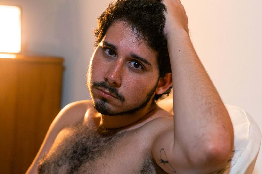 Homem sentado em frente a uma parede, iluminado por uma fonte de luz direta.