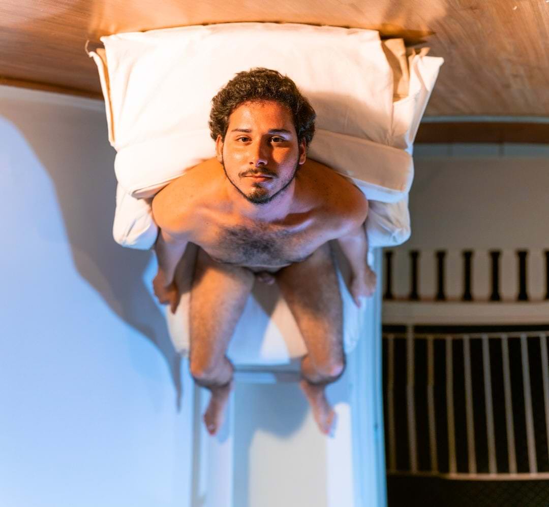 Pessoa de costas sobre a cama, com luz suave no teto e paredes laterais visíveis.