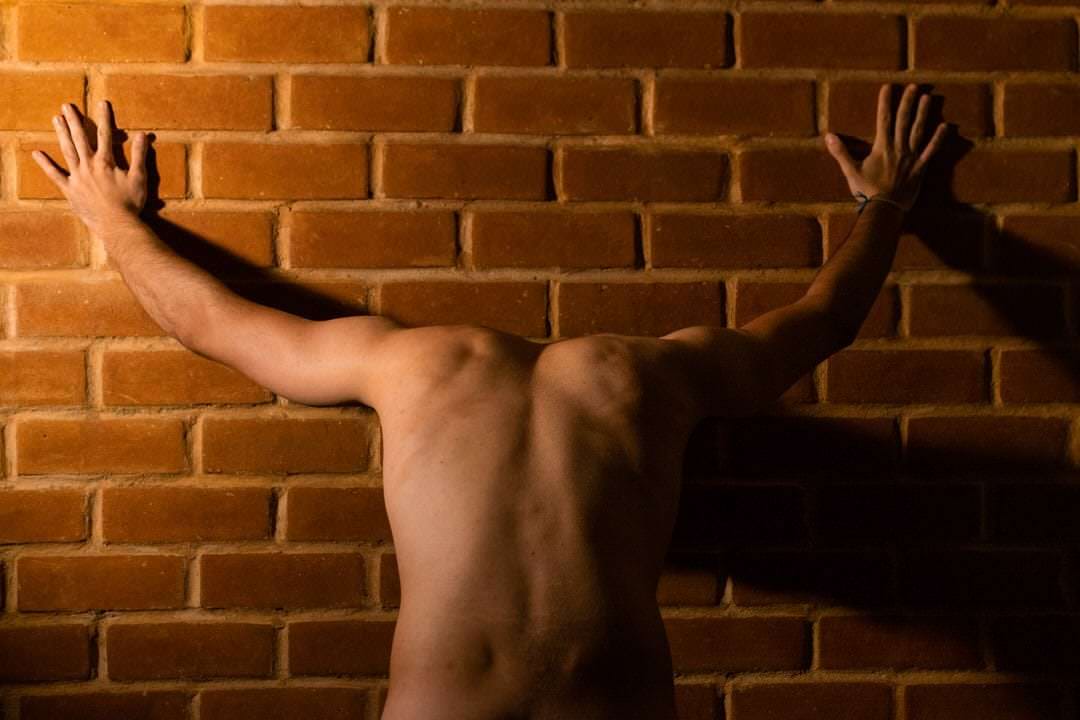 Pessoa em pé diante de um muro, luz natural difusa no fundo.