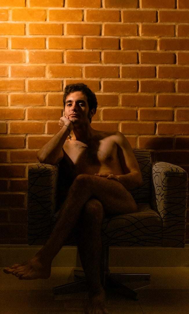 Pessoa sentada em sofá, fundo com parede de tijolo. Luz natural suave, composição equilibrada.