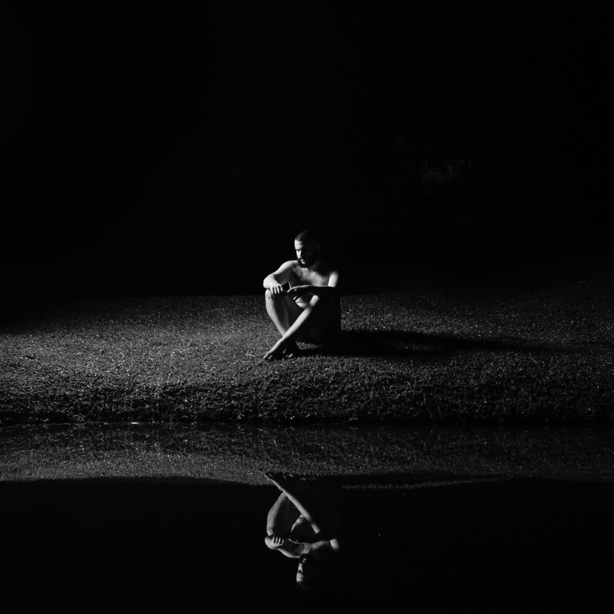 Pessoa sentada no chão, olhando para a câmera, em ambiente com luz natural difusa e fundo desfocado.