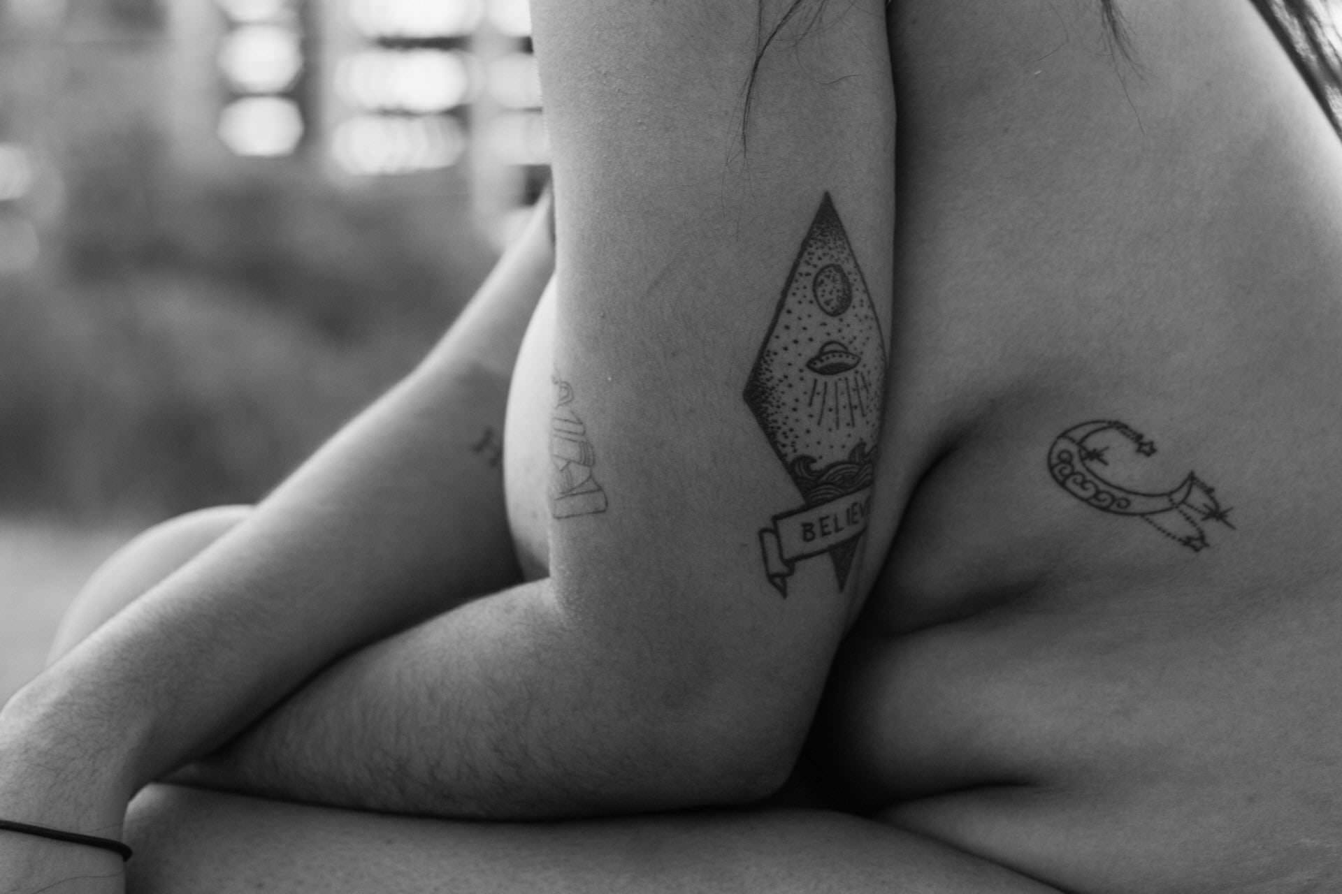 Pessoa com tattoos visíveis em corpo, fundo desfocado.