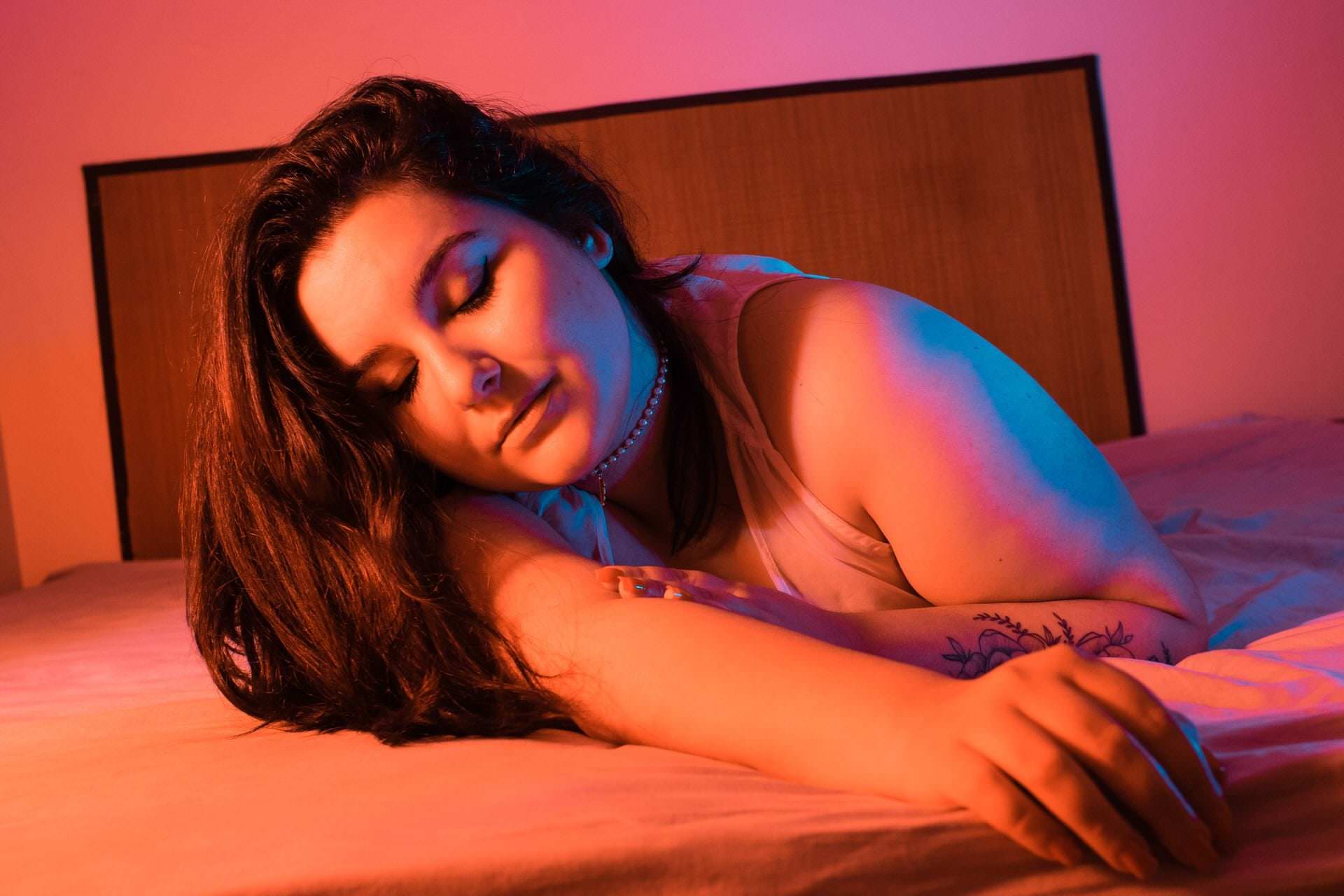 Uma mulher de costas está deitada em uma cama, segurando um colar.