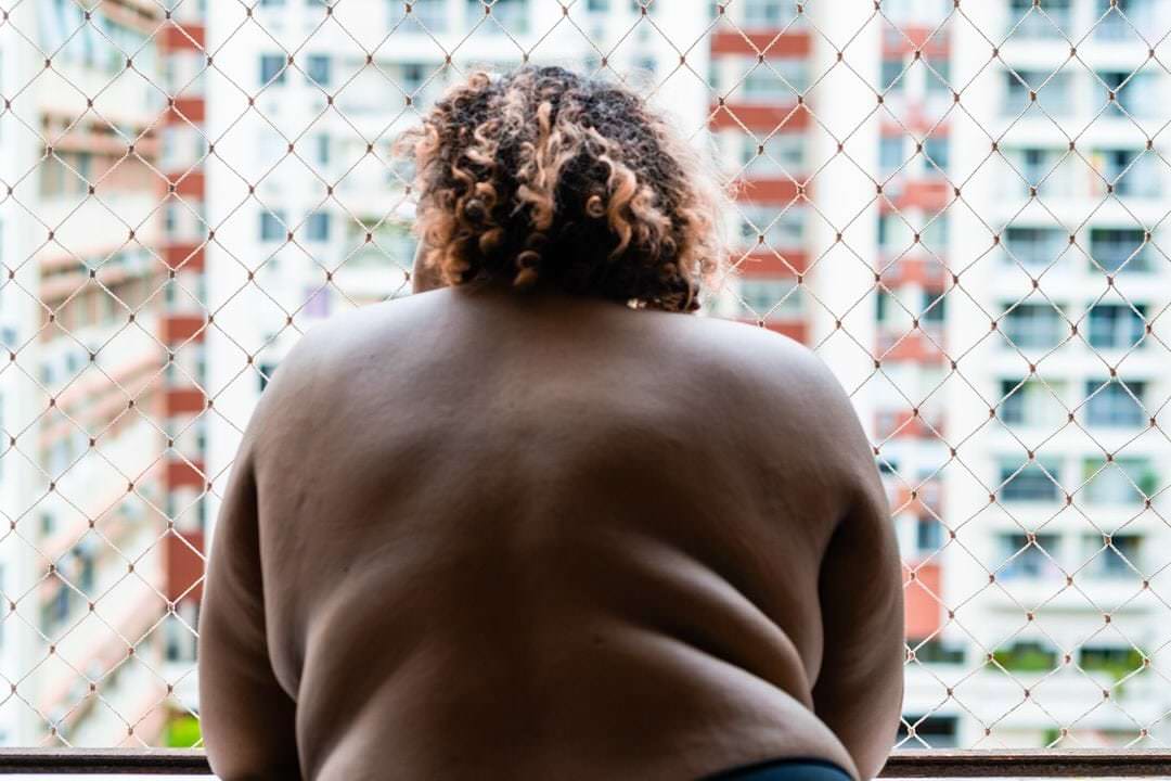 Um indivíduo está em um espaço com fundo de malha, iluminação natural suave e composição equilibrada.