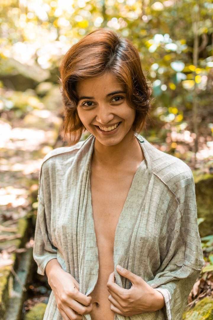 Uma mulher sorridente, de costas para a câmera, em frente a árvores verdes com luz natural difusa.