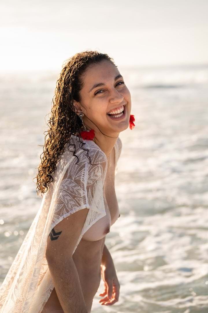 Uma mulher de costas, em posição ereta, frente a um fundo de água reflexiva e suave.