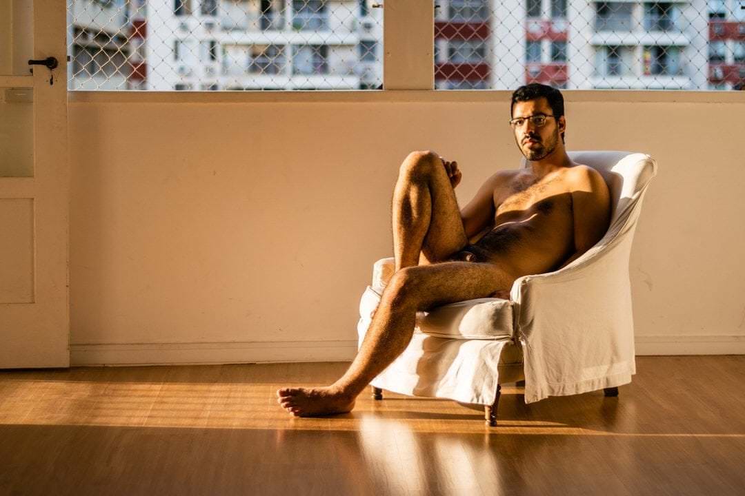 Pessoa sentada em cadeira, frente para uma parede e janela com luz natural saindo do vidro.