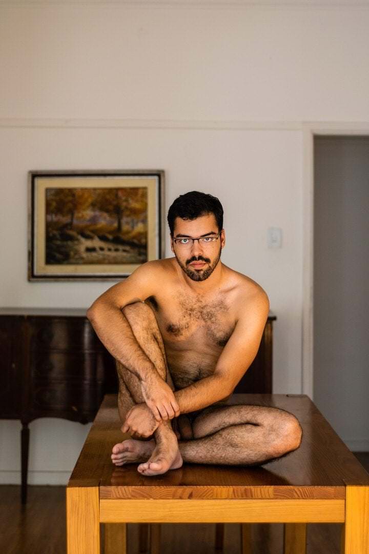Pessoa sentada em uma mesa, com luz natural vinda da janela, fundo com quadro preso na parede.