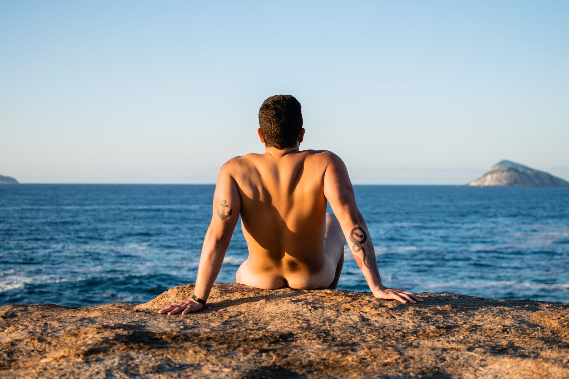 Pessoa sentada em pedra, com água e céu de fundo, luz natural suave e composição equilibrada.