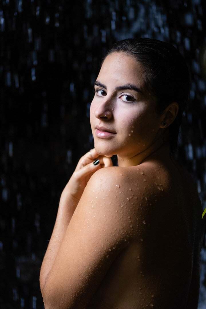 Uma mulher sentada em um banco de madeira, olhando para a frente, sob luz natural suave e difusa.