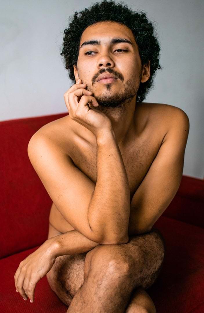 Pessoa sentada em sofá, com fundo de parede. Luz natural suave, composição equilibrada.