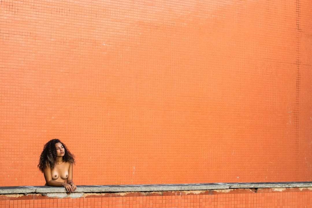 Uma mulher sentada em frente a uma parede, luz natural saindo do canto superior direito.