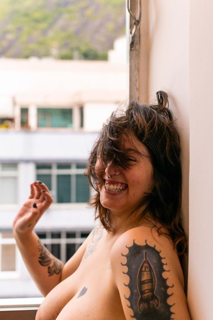 Uma mulher sentada em um prédio, com árvores no fundo e luz natural saindo do lado direito.