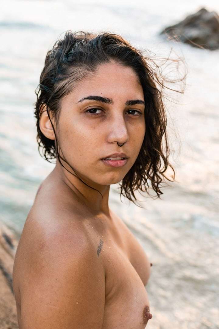 Uma mulher sentada em um banco, olhando para a frente, com fundo desfocado.