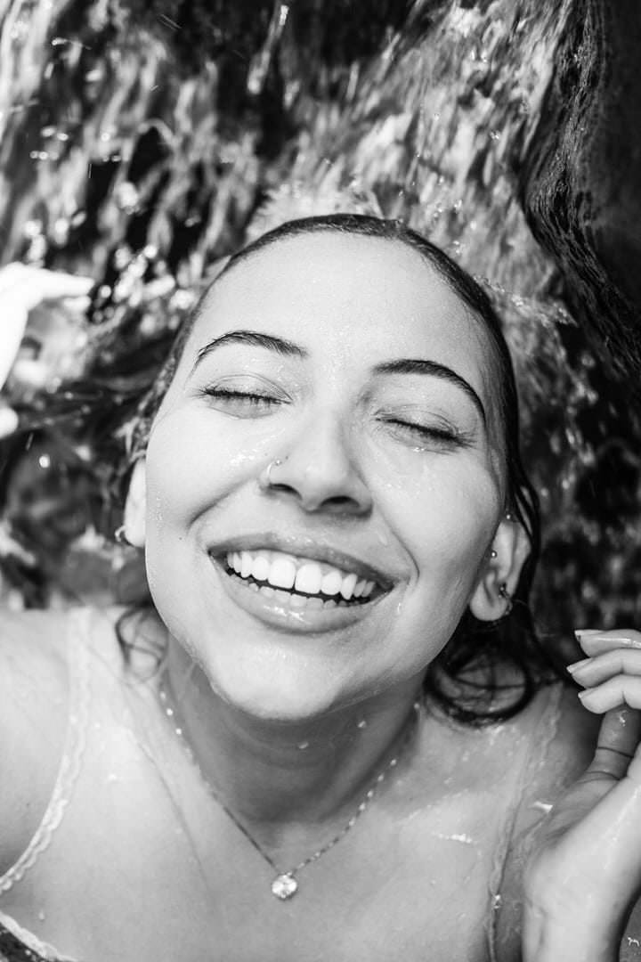 Uma mulher sorrindo em um ambiente escuro, com luz suave vindo de um canto.