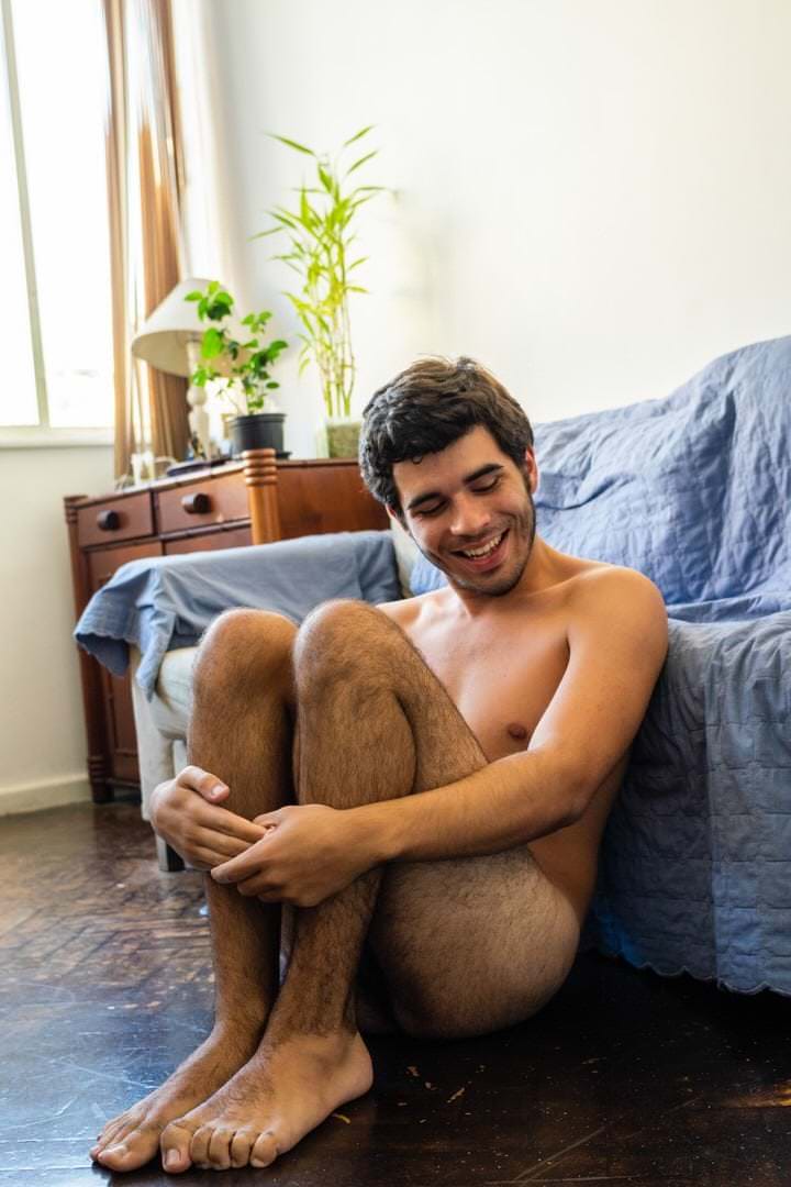 Pessoa sentada no chão, com um lampião e uma planta visíveis no fundo, luz natural saindo da janela.