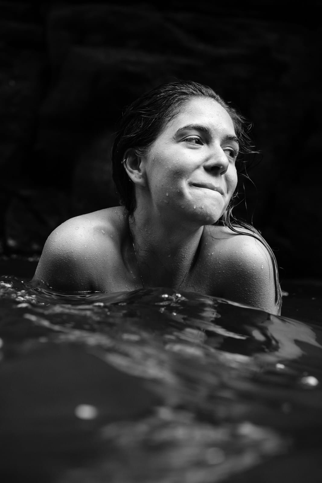 Uma mulher está nadando em um lago, com o céu escuro e luz difusa, retratada em preto e branco.
