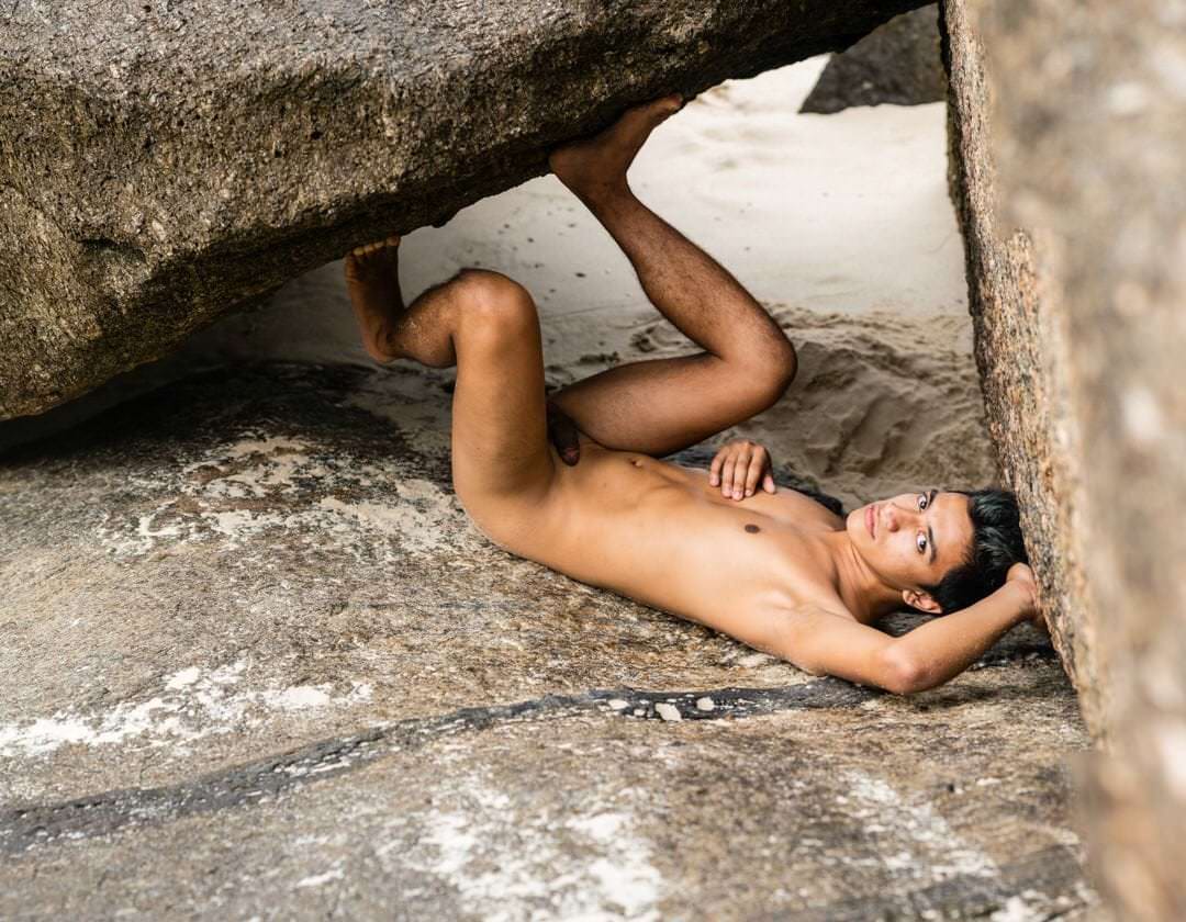 Pessoa de costas sobre o chão, próximo a uma pedra e a uma parede. Luz natural difusa, composição simples.
